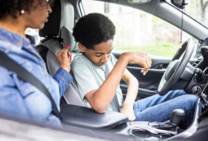 A teen driver is pictured here buckling up before heading out while his mother looks on from the front passenger seat.