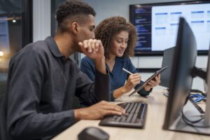 what-data-says Two young workers -- one male and one female -- sit at a desk and work to support each other on a data entry project.
